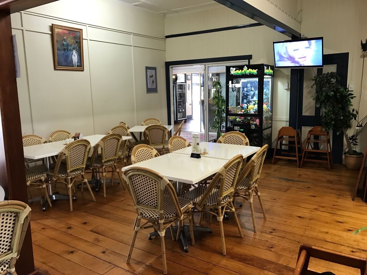 A restaurant with wooden flooring, wicker tables and chairs, a television, and a vending machine.