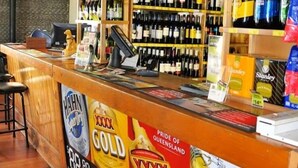 A bar area with a counter displaying various alcoholic beverages, a cash register, and a sign promoting a local pride. - Exchange Hotel Toogoolawah (Toogoolawah)