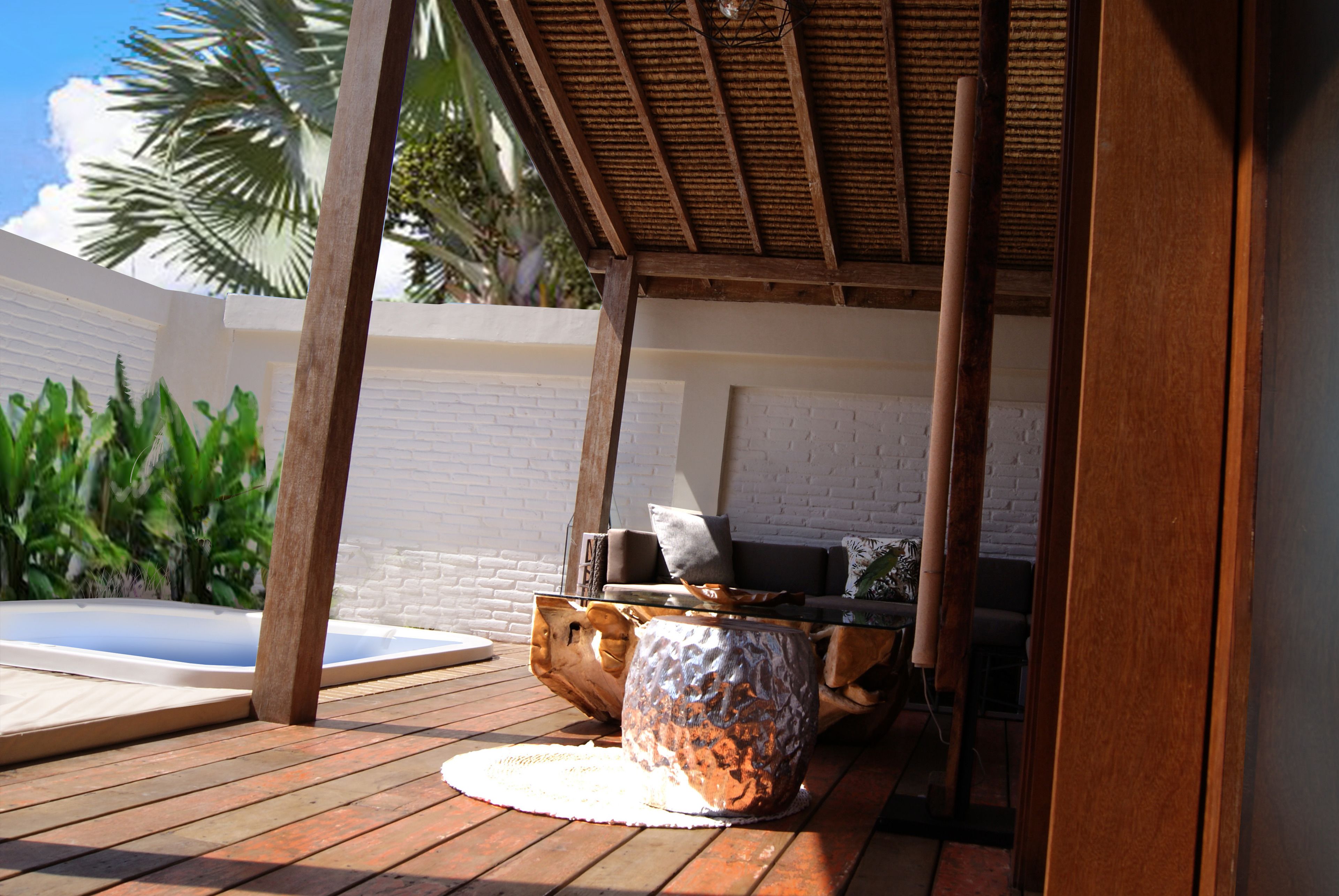 A wooden deck with a hot tub, a rustic table, and a white brick wall.
