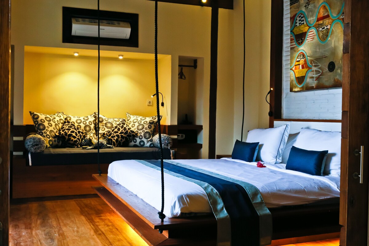 A modern hotel room with a bed, a sofa, and a wall-mounted air conditioner.