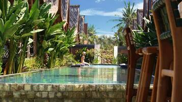 A swimming pool with a stone border, surrounded by tropical plants and wooden structures.