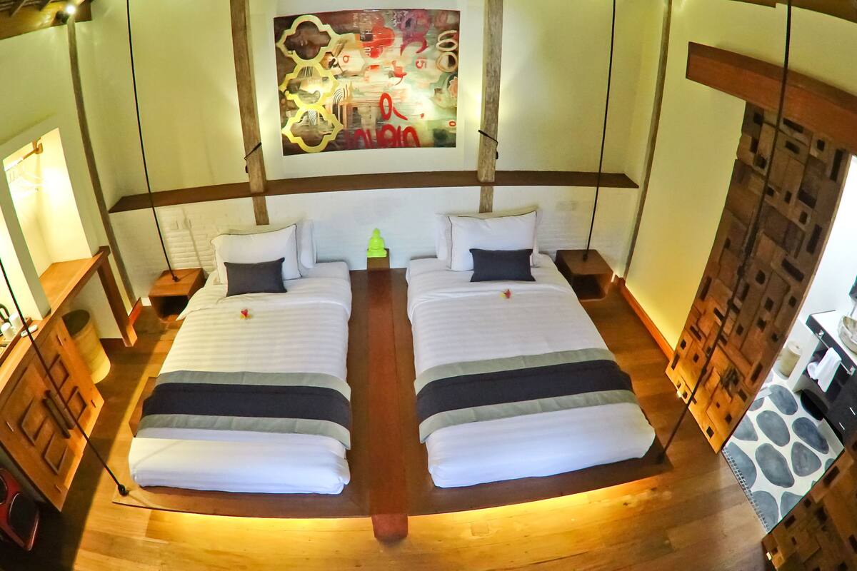 Een tweepersoonsbed met een houten hoofdbord, een klein nachtkastje met een lamp, en een schilderij aan de muur.