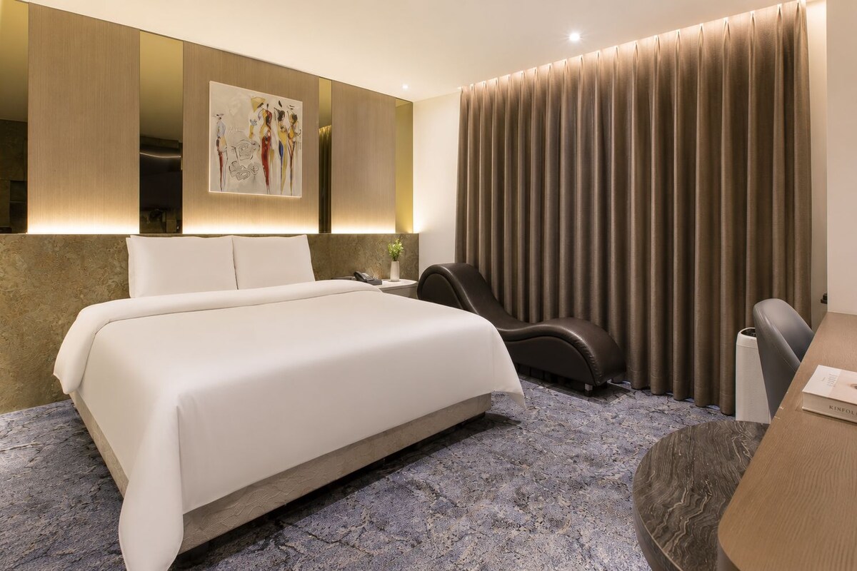 Une chambre d’hôtel moderne dotée d’un grand lit, d’un fauteuil massant, d’un bureau et d’une grande fenêtre avec des rideaux.
