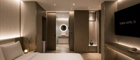 A modern hotel room with a bed, bedside table, TV, and a view into the bathroom.