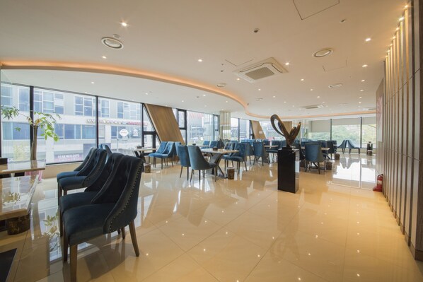 A modern hotel lobby with a spacious layout, large windows, and a central seating area with blue chairs and tables. - Guwol Hotel (Incheon)