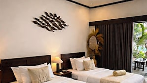 Habitación de hotel con dos camas, un ventanal con vistas a palmeras, un adorno en la pared y una mesita de noche con lámpara.