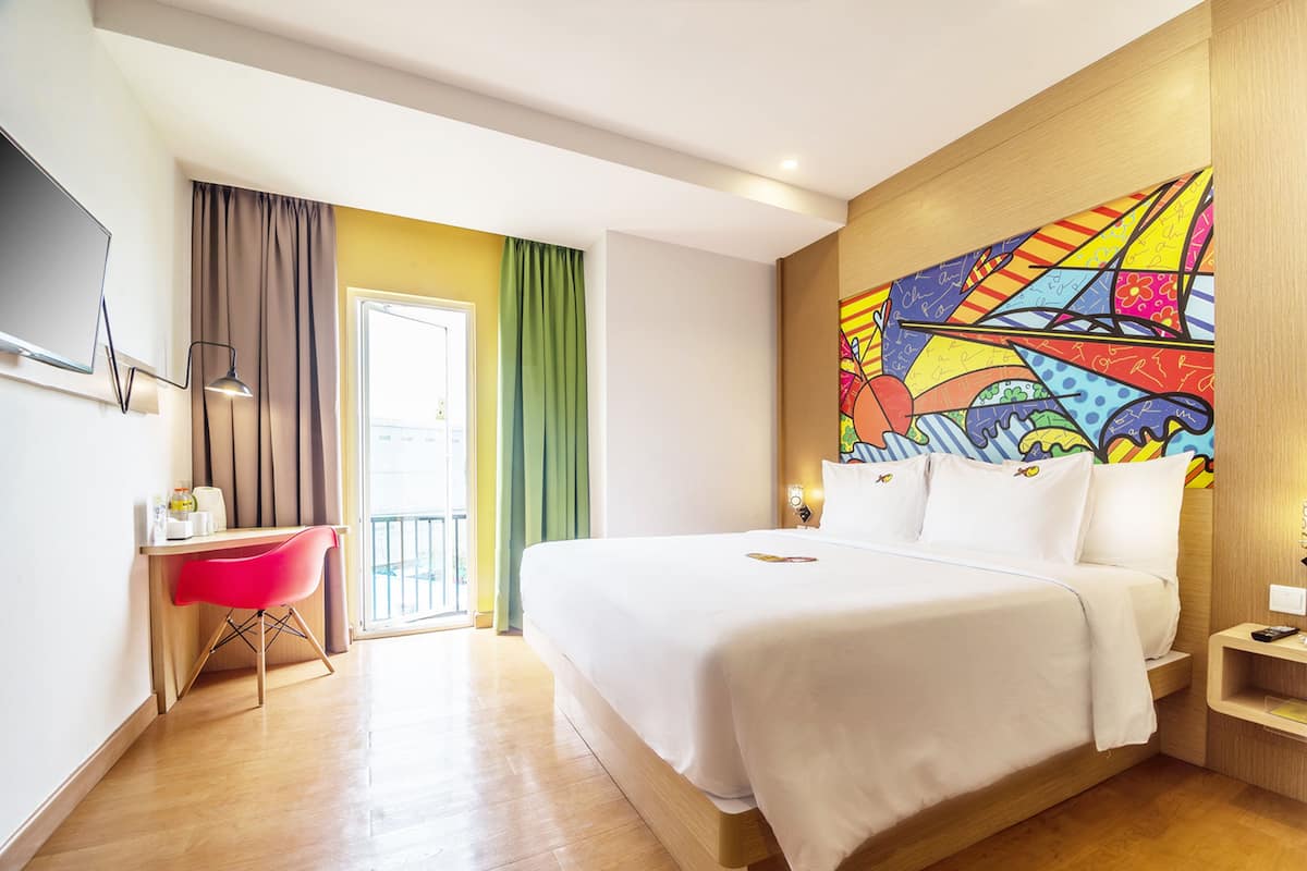 Ein Hotelzimmer mit Bett, Schreibtisch, Stuhl, Fernseher und einem farbenfrohen Wandgemälde.