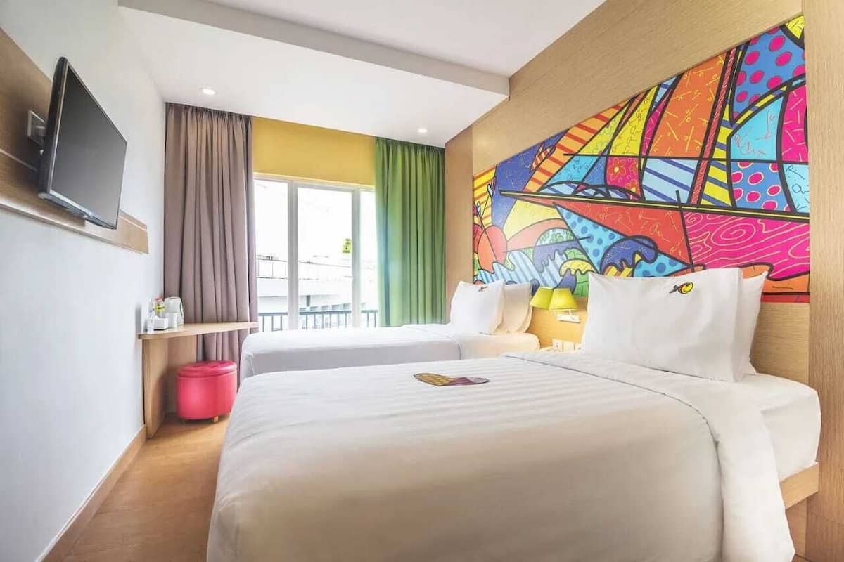 Ein Hotelzimmer mit zwei Betten, einem Fernseher, einem farbenfrohen Wandbild und Blick nach außen.