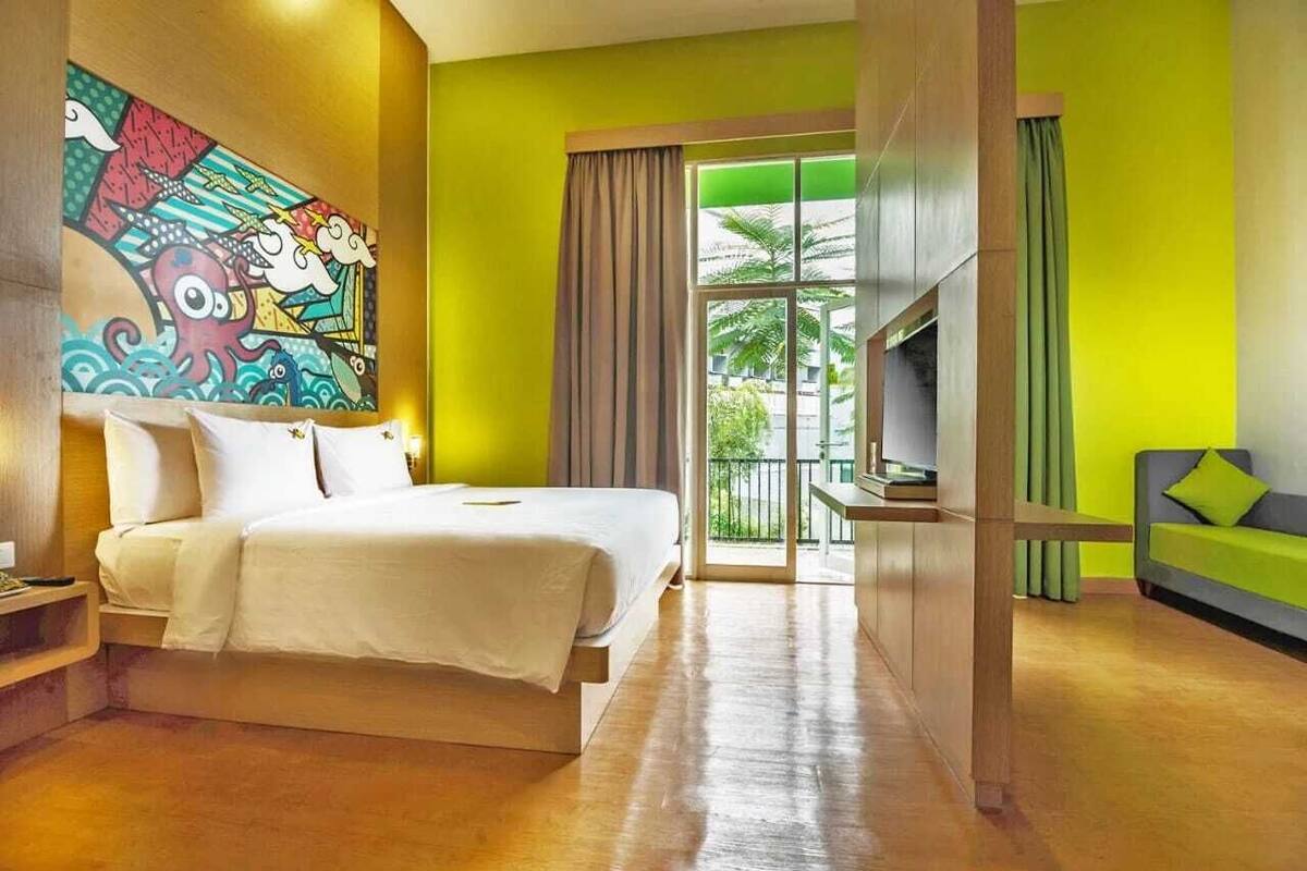 Ein Hotelzimmer mit Bett, Fernseher, Sofa und einem farbenfrohen Wandgemälde.