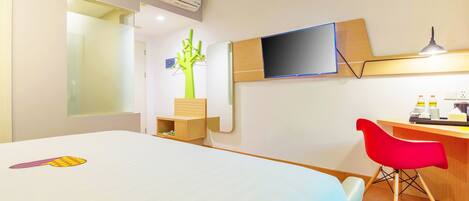 Ein Hotelzimmer mit Bett, Schreibtisch, rotem Sessel, Fernseher und Pflanze.