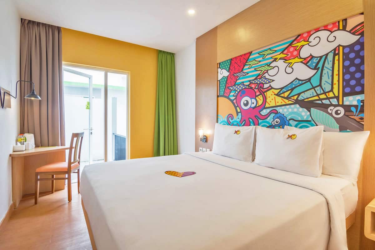 Ein Hotelzimmer mit einem Bett, einem Schreibtisch und einem farbenfrohen Wandgemälde.