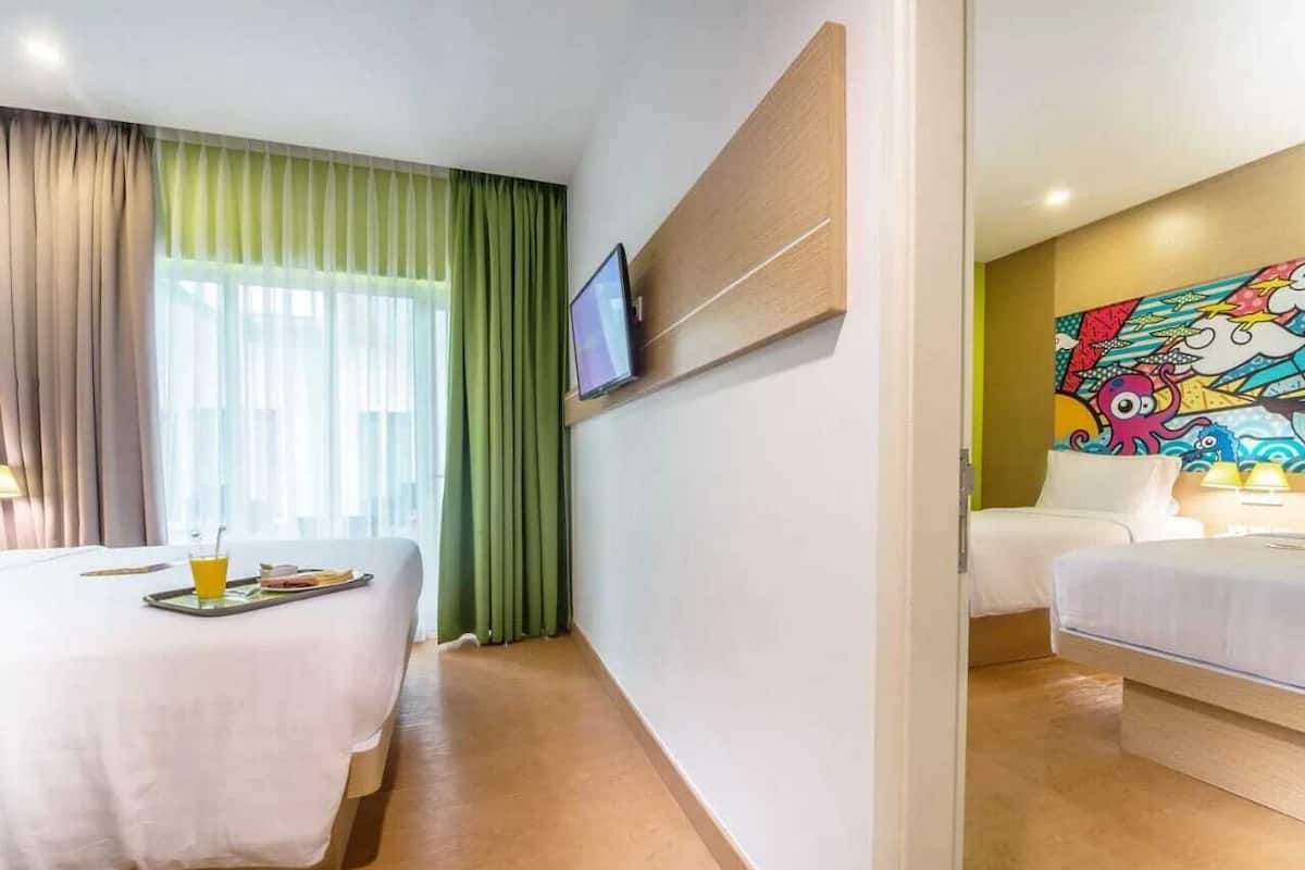 Ein Hotelzimmer mit Bett, einem an der Wand montierten Fernseher, einem Bild und einem Fenster mit Vorhängen.