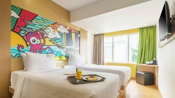 A hotel room with two beds, a colorful mural on the wall, a TV mounted on the wall, and a window with green curtains.