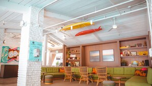 A spacious lounge area with a green sofa, wicker chairs, and a small table. - The Surfjack Hotel & Swim Club (Honolulu)