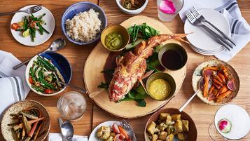 A wooden table with various dishes including rice, vegetables, and a roasted fish.