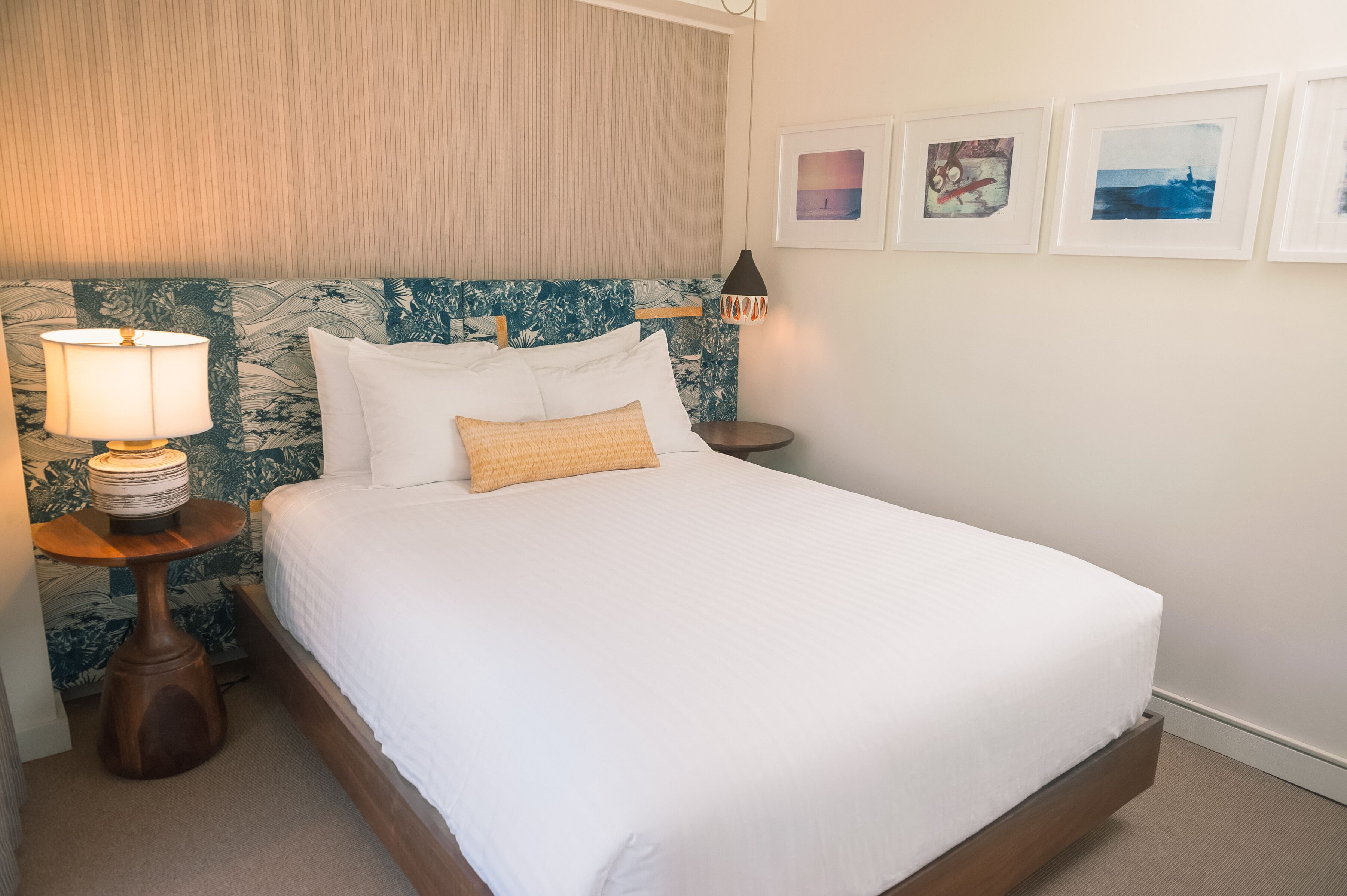 A neatly made bed with white linens and a single decorative pillow, a bedside lamp, and a small wooden table with a lamp.