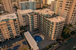 A high-rise hotel with multiple balconies, a rooftop pool, and a parking area.