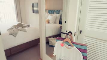 Camera d'albergo con un letto, uno specchio che riflette l'ambiente, un armadio e un appendiabiti con abiti.