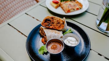 A plate with a burrito, a small bowl of sauce, and a small bowl of sour cream on a table.