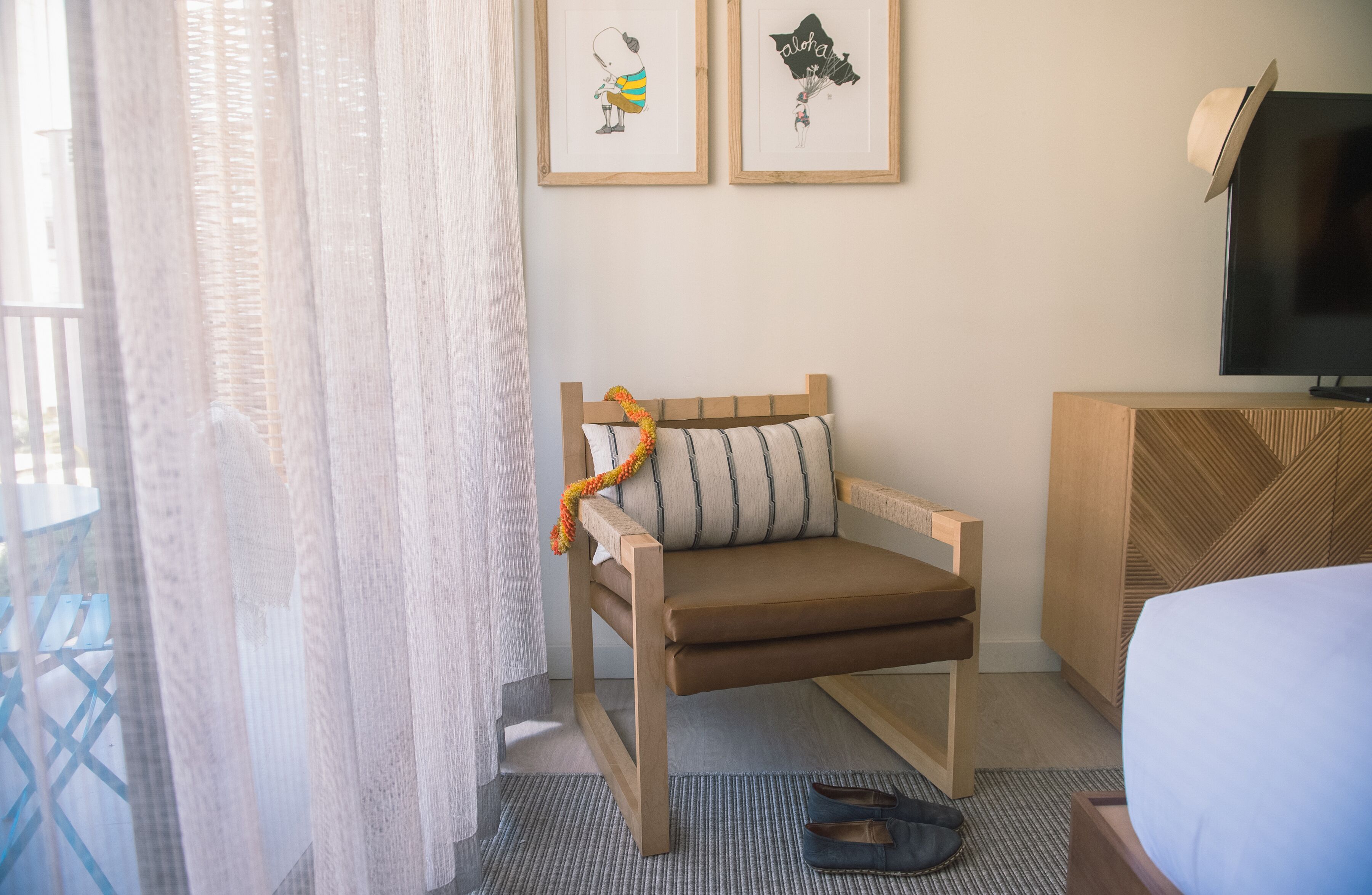 Une chambre d’hôtel avec une chaise en bois, un lit, un téléviseur et deux tableaux encadrés au mur.