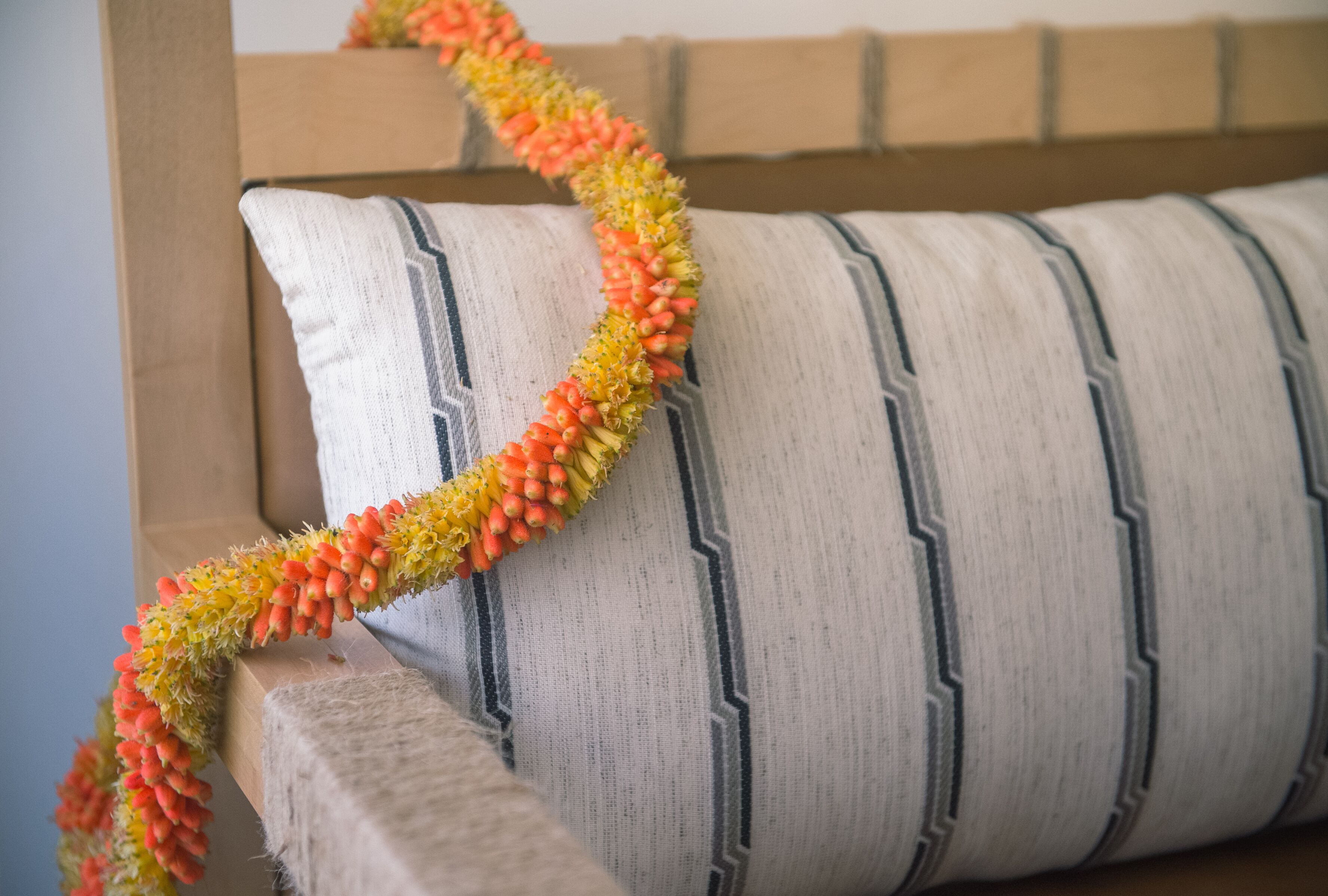 Una cama con un cojín a rayas y una guirnalda de flores naranjas y amarillas.