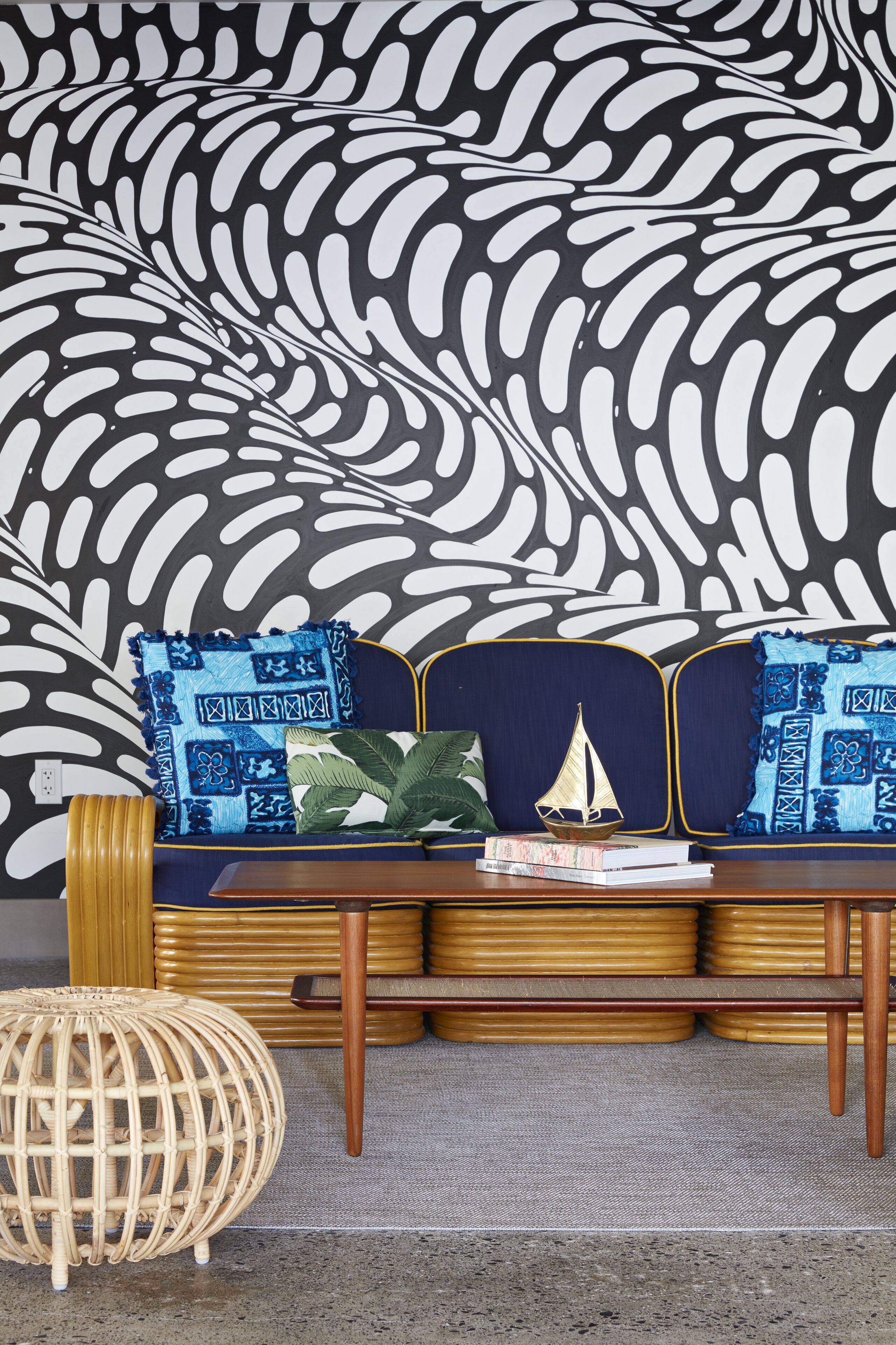 A sofa with blue and white patterned cushions, a small sailboat decoration, and a woven stool.