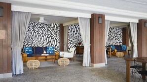 A modern hotel lobby with a seating area featuring a sofa and chairs, a wooden table, and a patterned wall. - The Surfjack Hotel & Swim Club (Honolulu)