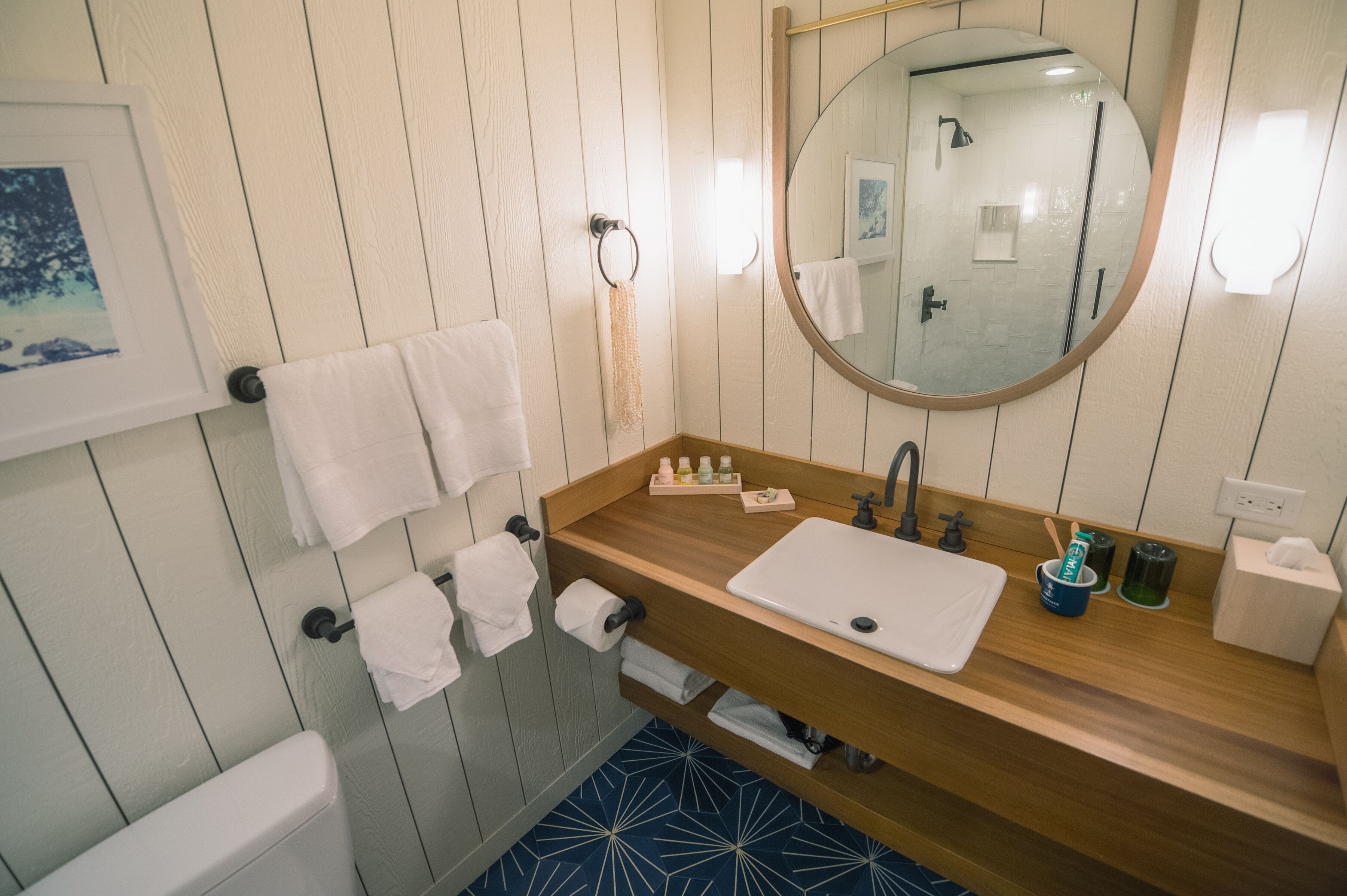 Une salle de bain avec un meuble-lavabo en bois, un lavabo blanc et un grand miroir. On peut voir des serviettes suspendues à un porte-serviettes et des toilettes.