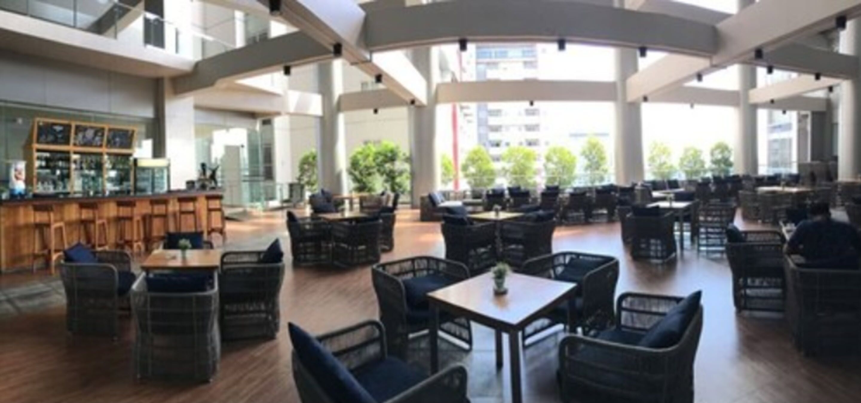 Um espaço amplo e interno com vários arranjos de assentos, incluindo mesas e cadeiras, e um bar à esquerda.