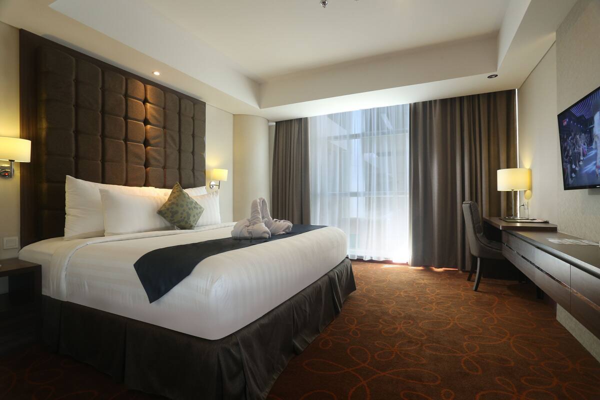 Habitación de hotel con una cama grande, un escritorio, una silla y un televisor en la pared.