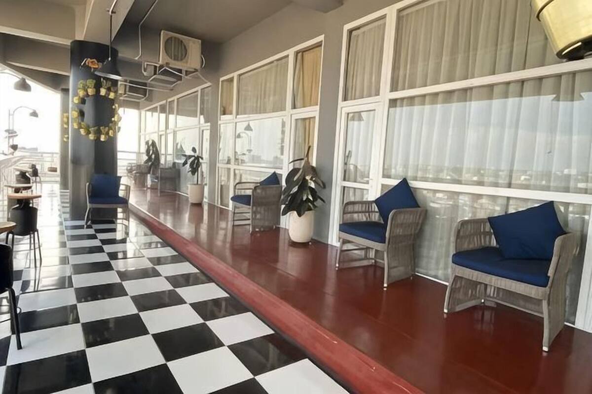 Un largo pasillo con piso a cuadros, sillas de mimbre con cojines azules y ventanas amplias.