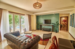 Una sala de estar con sofá, televisor, mesa de comedor, sillas y una planta en maceta.