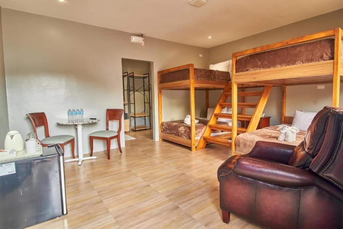 Habitación tipo dormitorio con literas, un pequeño rincón de cocina, una mesa de comedor con sillas y un sofá de cuero.