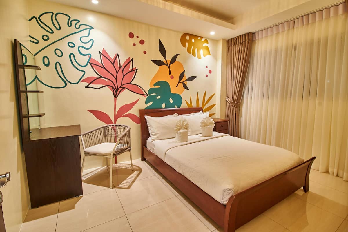 Un dormitorio moderno con una cama de madera, una silla, un escritorio pequeño y un mural en la pared.