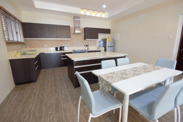A modern kitchen with dark cabinets, a central island, and a dining area with light blue chairs.