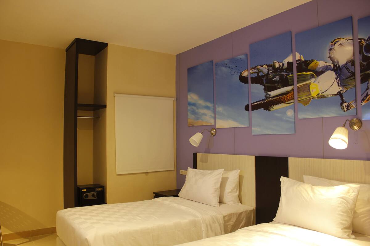 Een hotelkamer met twee bedden, een groot kunstwerk aan de muur, een whiteboard en een nachtkastje met een radio.