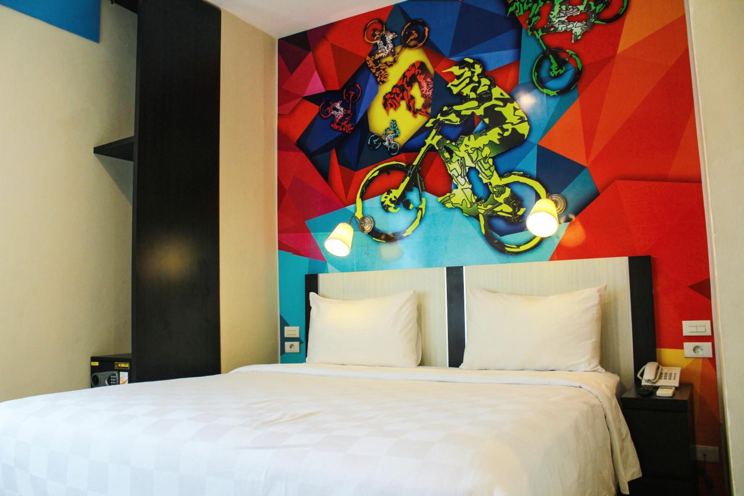 A hotel room with a bed, a nightstand with a phone, and a colorful wall mural.
