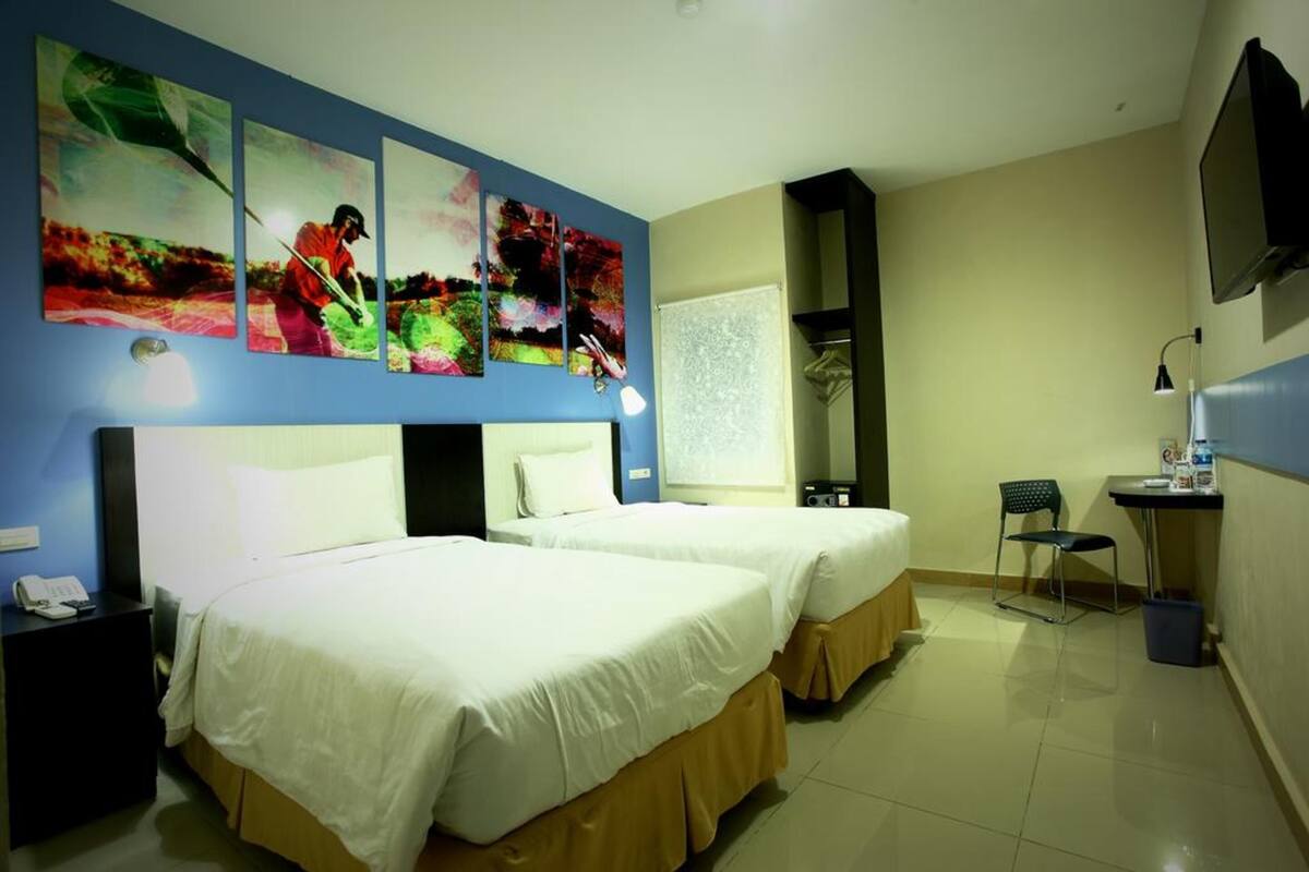 Een hotelkamer met twee bedden, een bureau, een stoel, een televisie en kunst aan de muur.