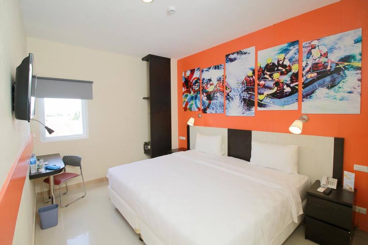 Hotelkamer met een bed, een bureau met stoel, een aan de muur bevestigde televisie en drie schilderijen die een roeiteam voorstellen.