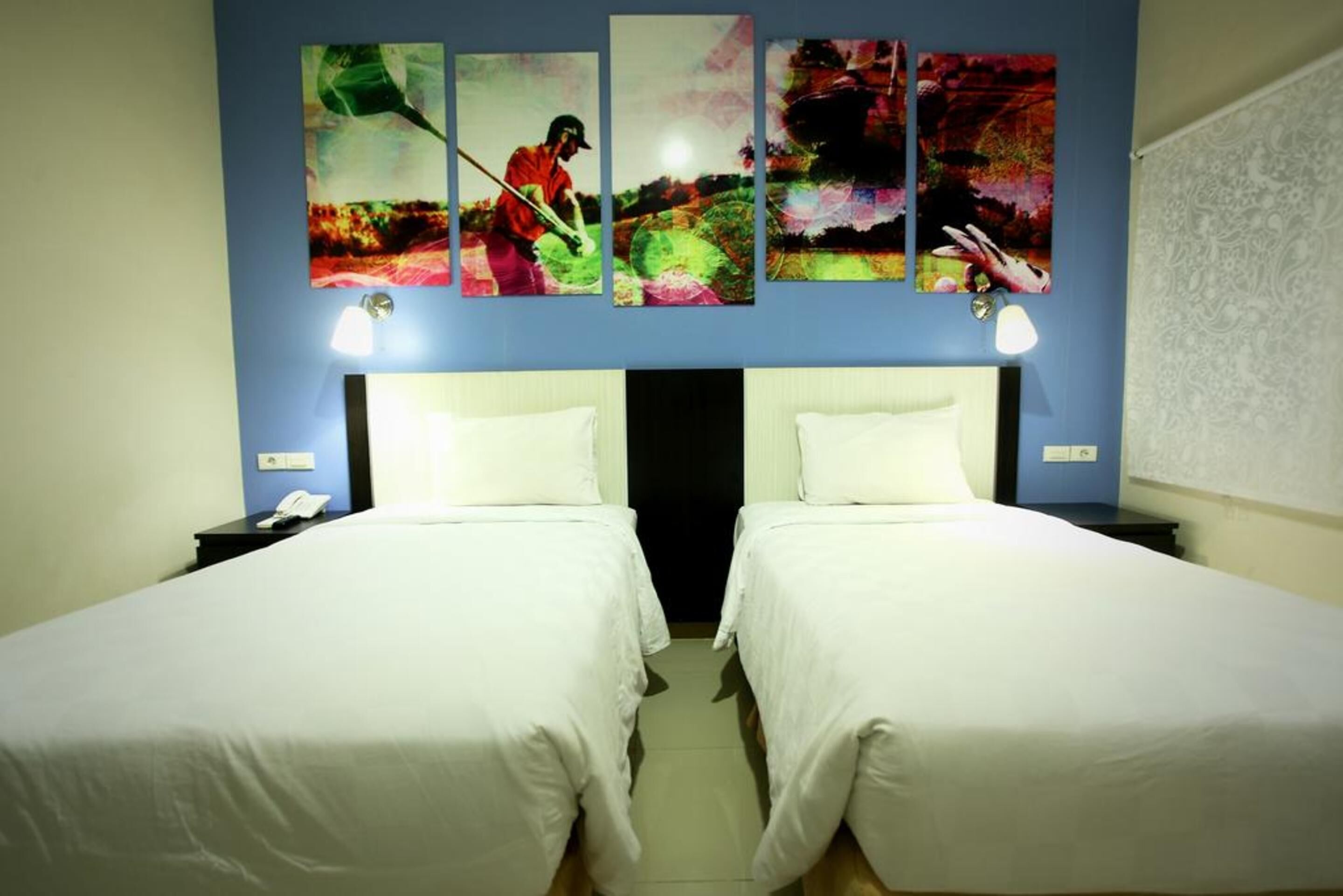 Une chambre d’hôtel avec deux lits simples, une table de chevet avec un téléphone et un mur orné de quatre tableaux colorés.