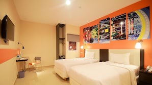 Quarto de hotel com duas camas, uma TV, uma escrivaninha com cadeira, um quadro na parede e uma mesa de cabeceira com telefone.