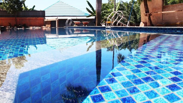 Visão nítida de uma piscina com azulejos azuis e reflexo de palmeiras.