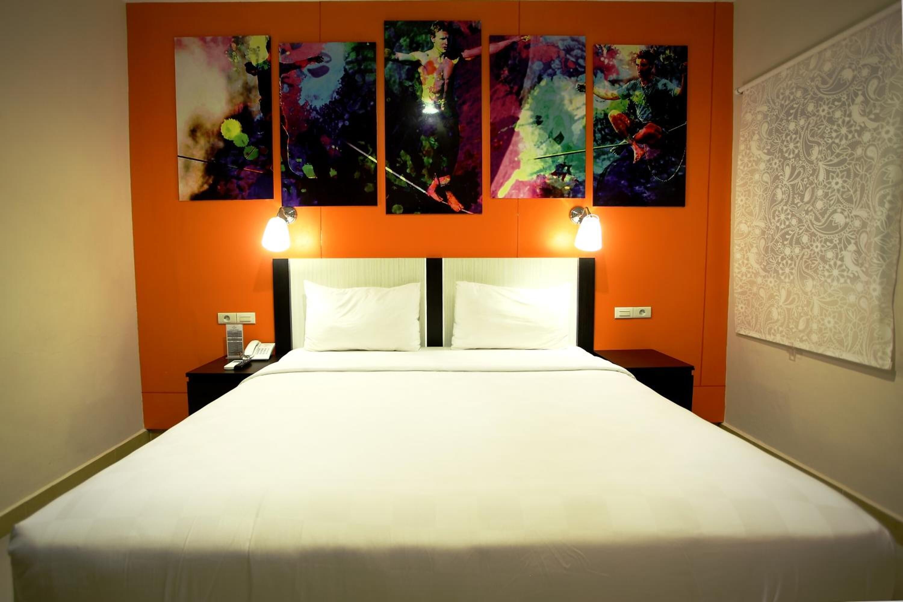 A hotel room with a large bed, two bedside tables, and three wall-mounted paintings.