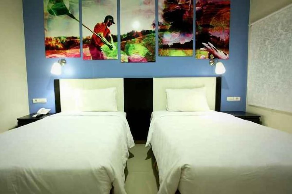 Een hotelkamer met twee bedden, een blauwe muur en een schilderij boven de bedden.