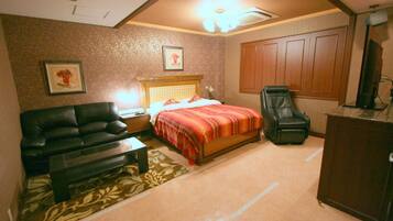 A bedroom with a bed, a black leather sofa, a wooden nightstand, a desk, a chair, and a wardrobe.