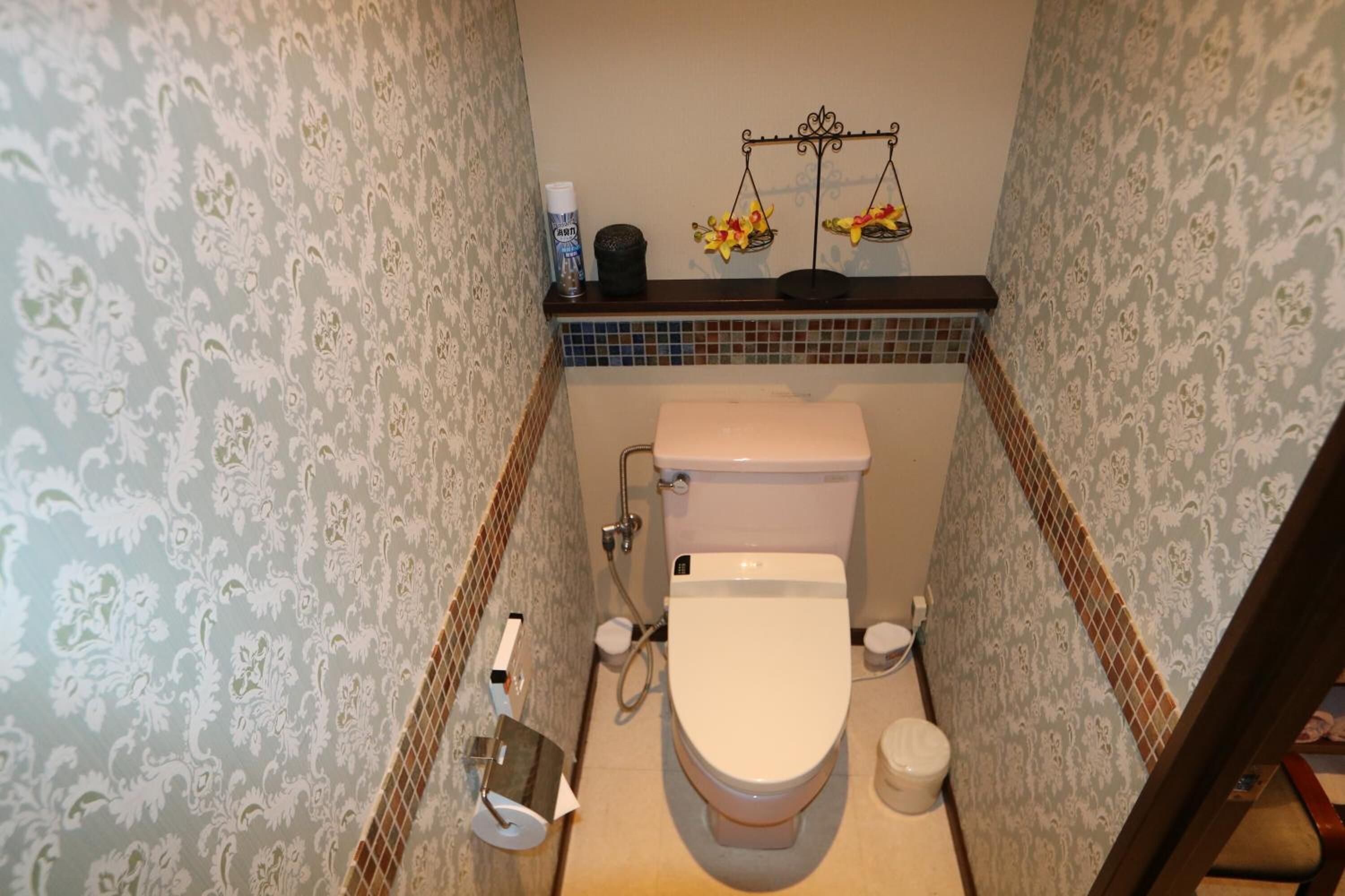 A bathroom with a toilet, bidet, and a small shelf with toiletries.
