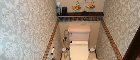 A bathroom with a toilet, bidet, and a small shelf with toiletries.