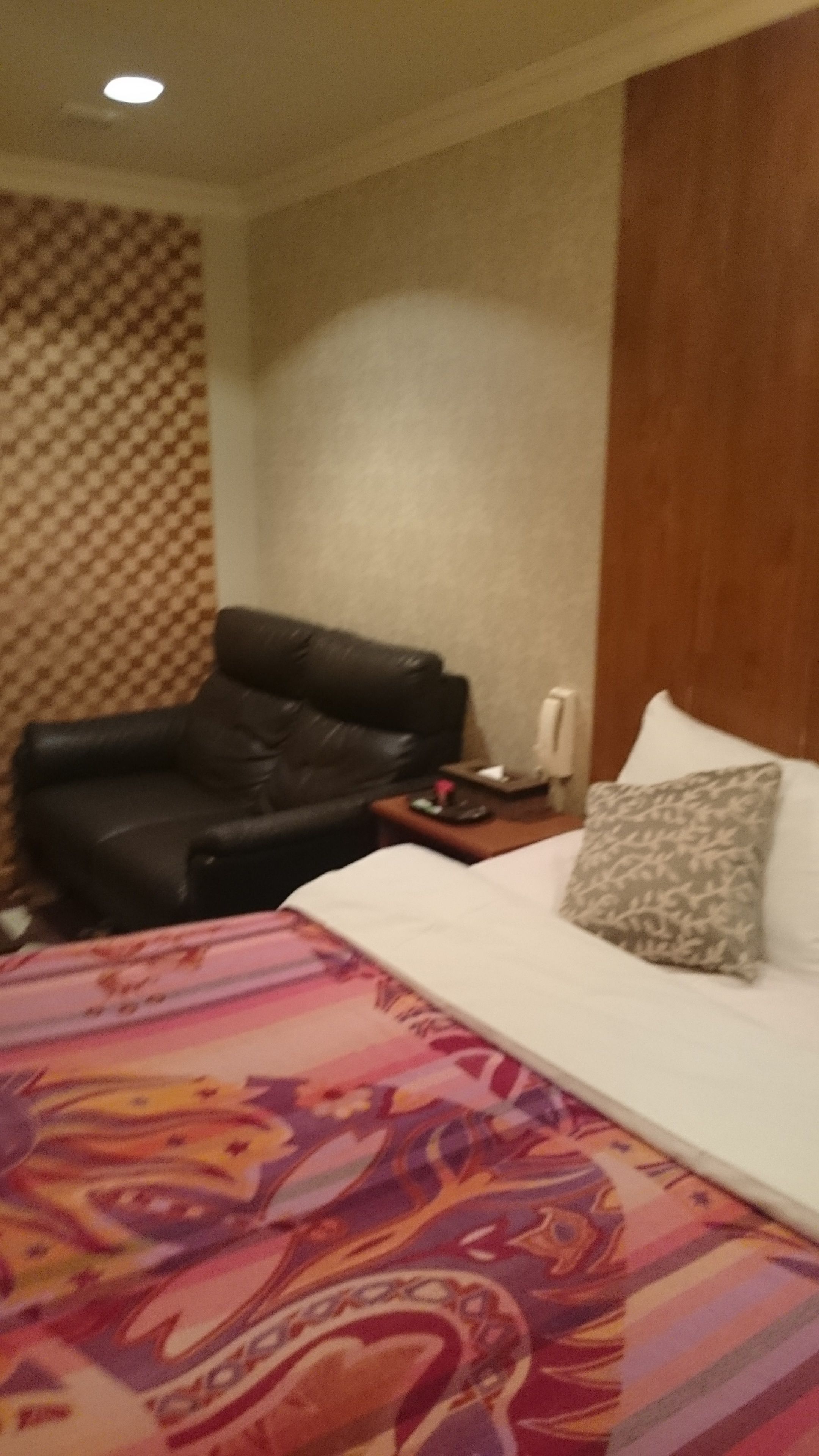 Ein Hotelzimmer mit einem Bett, einem schwarzen Ledersessel, einem Nachttisch und einer Wand mit Muster.