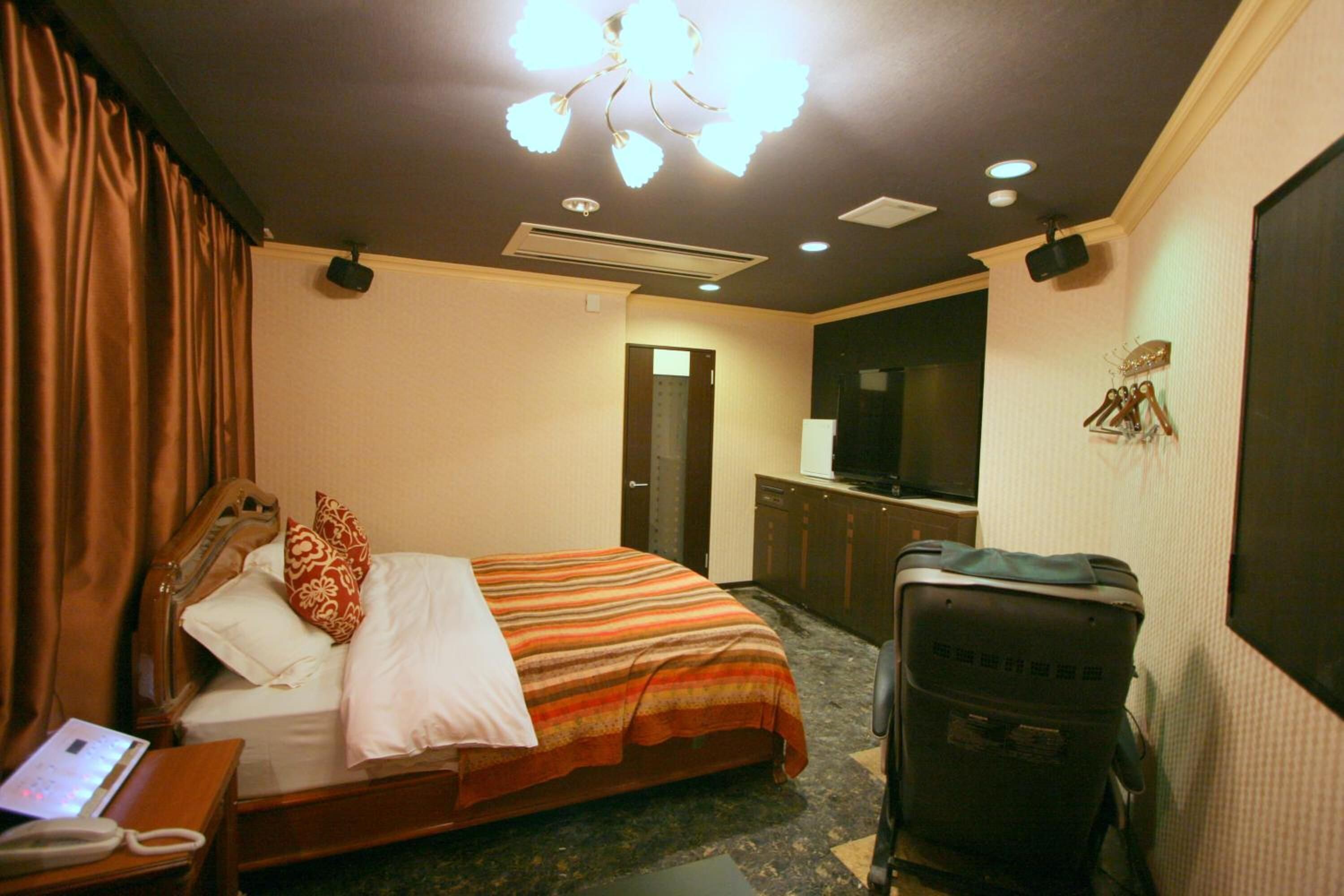 Une chambre d’hôtel avec un lit, un bureau avec un téléphone, une valise, un téléviseur et une porte donnant sur une autre pièce.