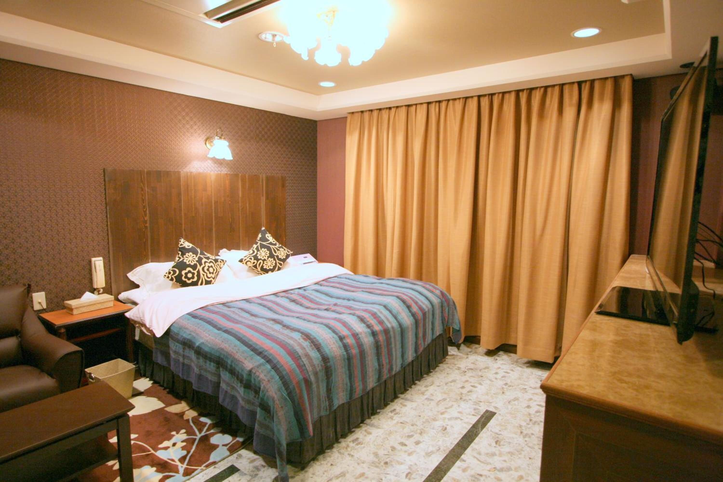 A hotel room with a bed, a desk, a chair, a nightstand, and a television.